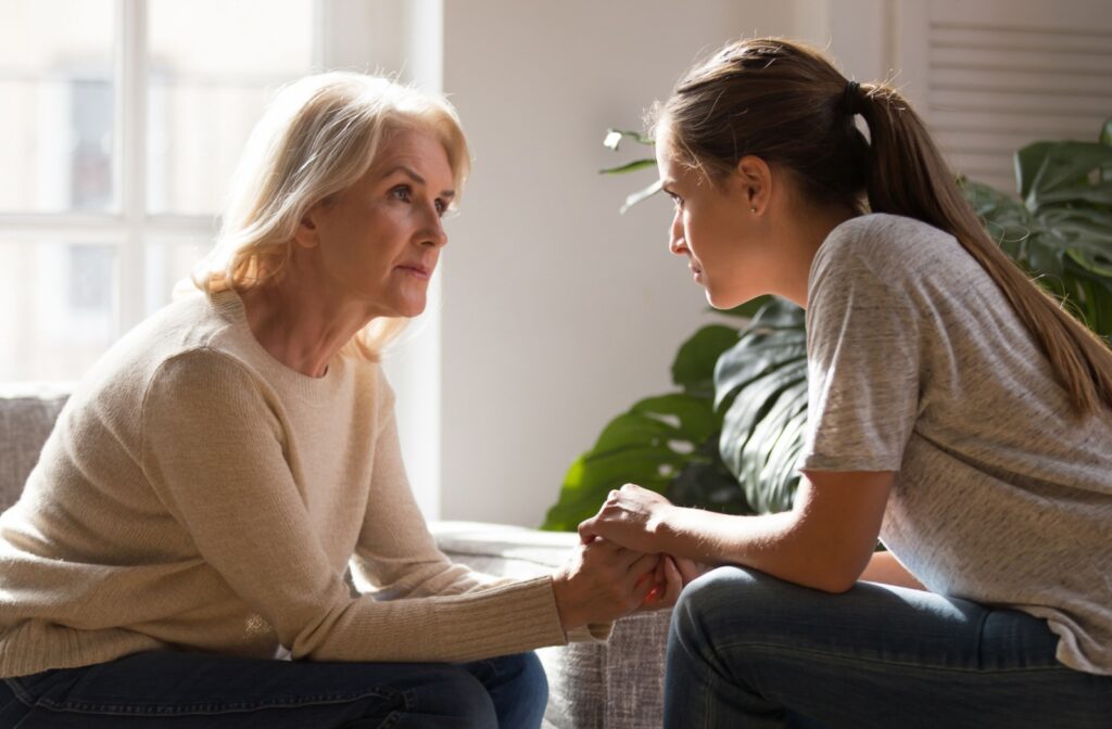 A young adult holds their older grandparent's hands and sits across from them during a serious conversation in memory care
