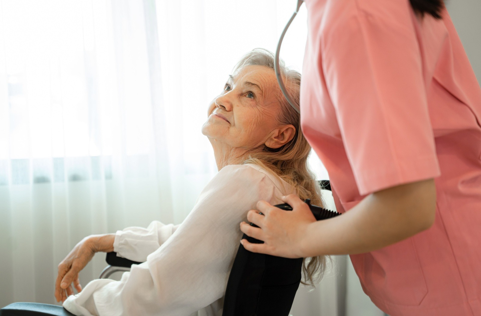 A memory care caregiver pushes a senior with cognitive decline in a wheelchair.