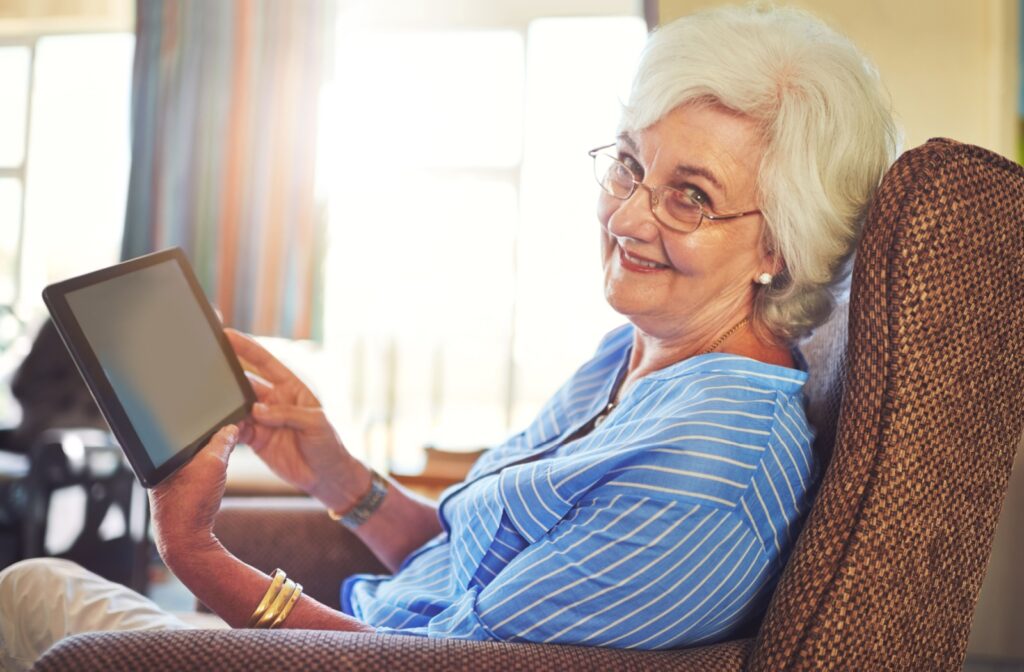 A senior living resident sits in an armchair while video calling a family member on a tablet.