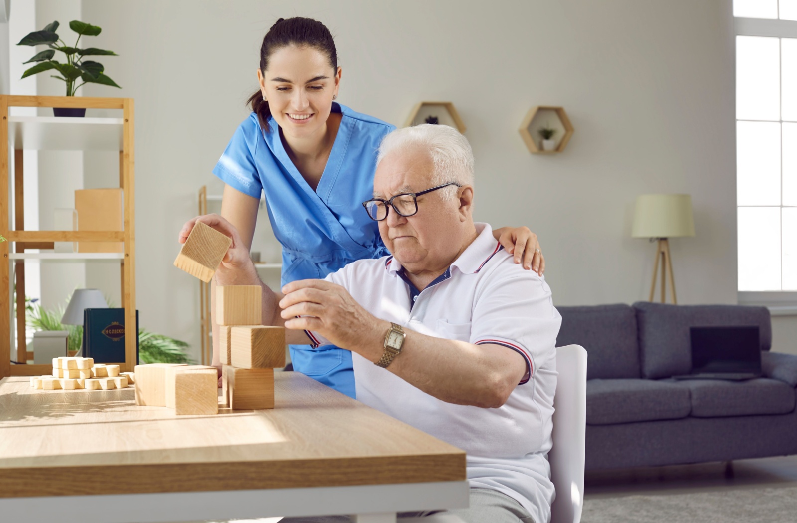 A caregiver assists a senior with dementia with a cognitive stimulation activity using wooden blocks.