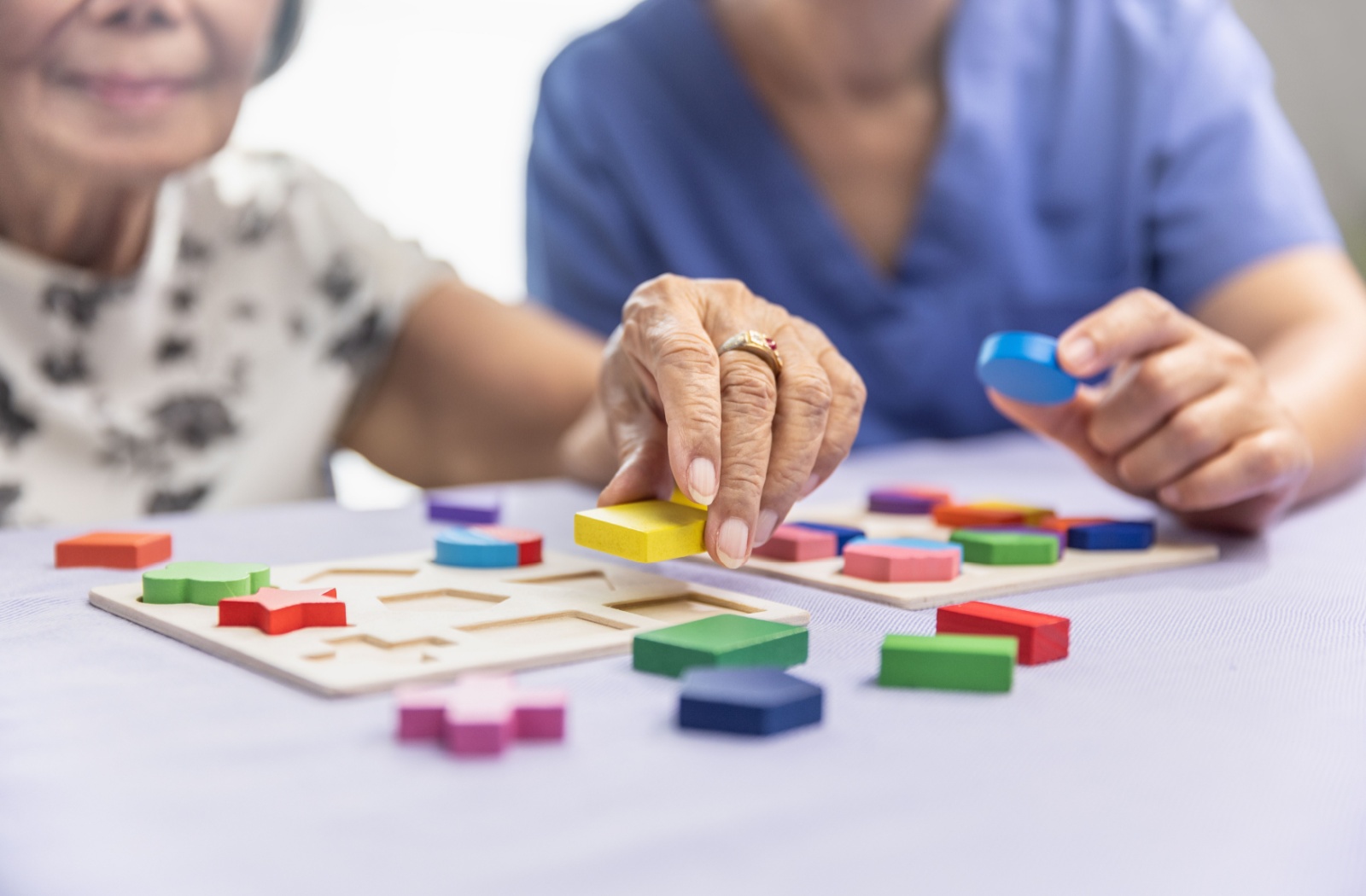A senior participates in a cognitive stimulation activity using colored shapes, with the guidance of a senior living caregiver.
