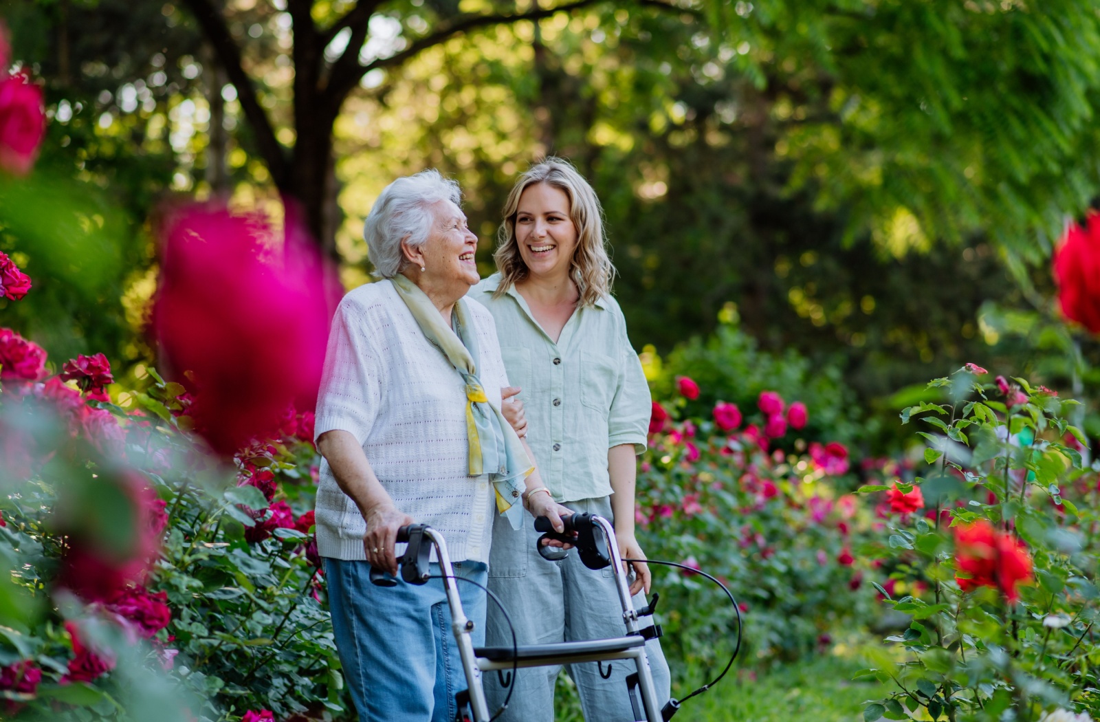 A senior in memory care enjoys a light stroll through a garden with flowers, as they chat with their adult grandchild.
